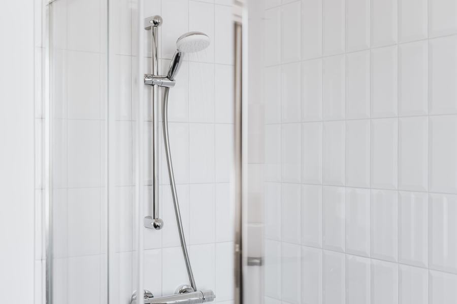 Douche à main chromée et barre murale dans une cabine aux carreaux blancs